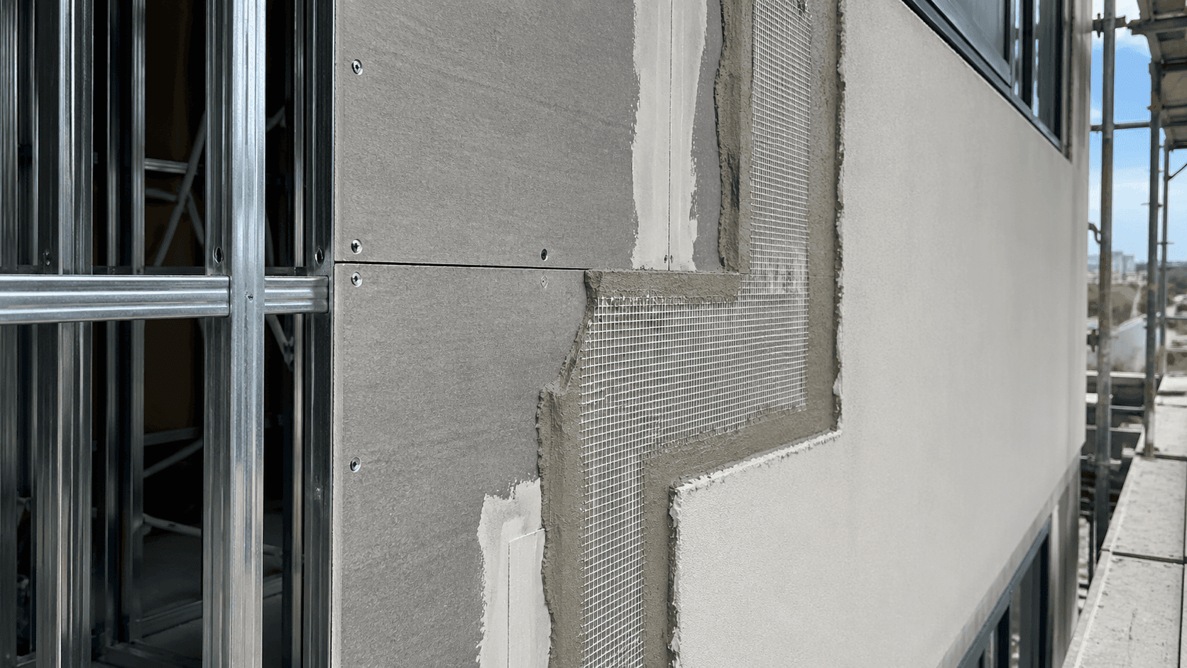 Fiber cement board installed behind a rendered wall system with visible metal studs, joint treatment, reinforcement mesh, and base coat.