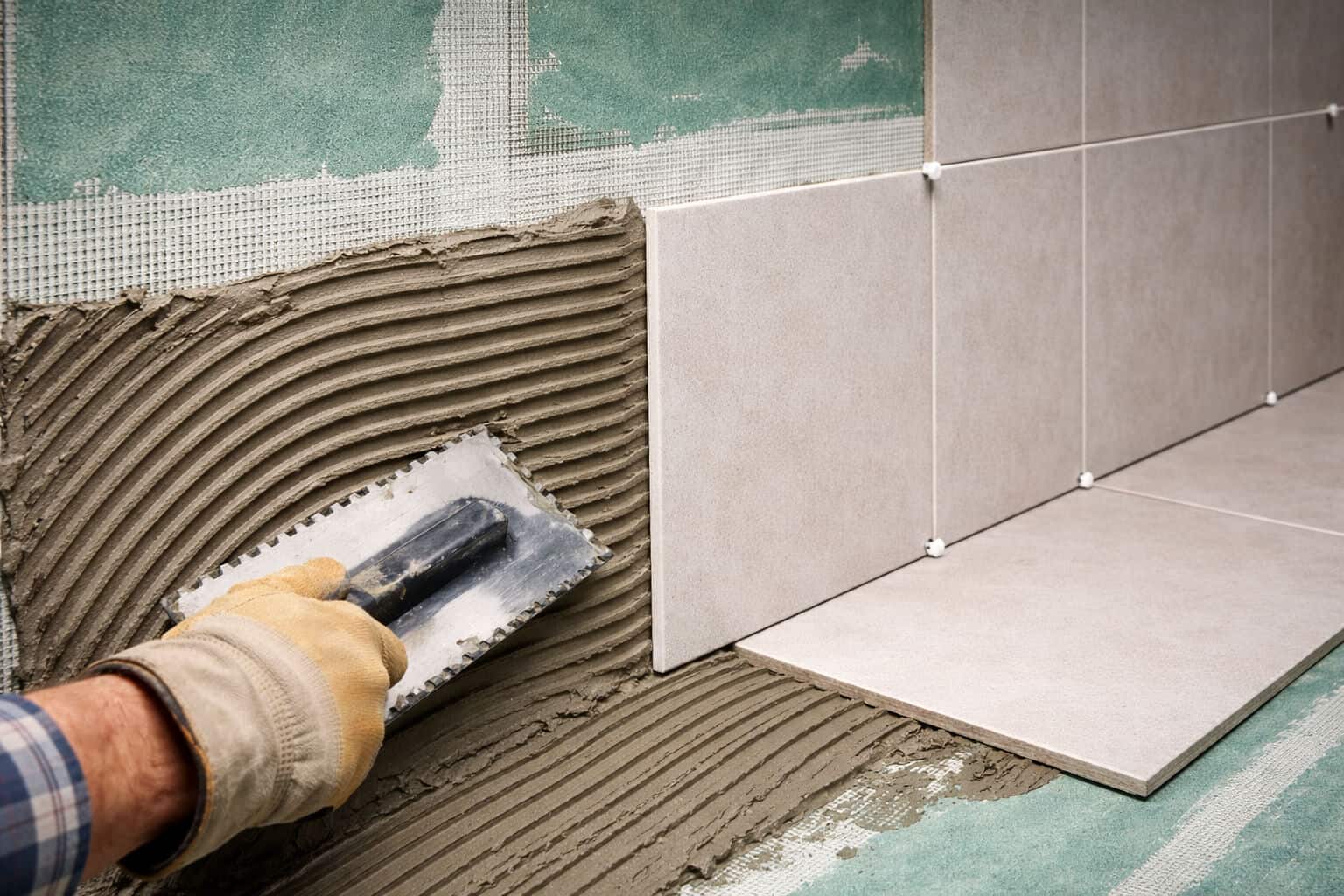 Applying tile adhesive over fiber cement boards with a notched trowel during wall tile installation in a wet area