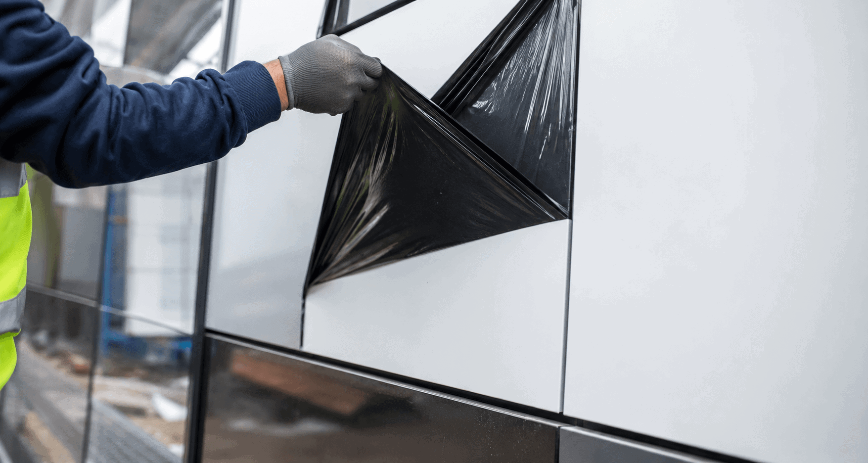 Worker removing protective film from an aluminium composite panel façade to prevent residue, scratches, and surface marks.