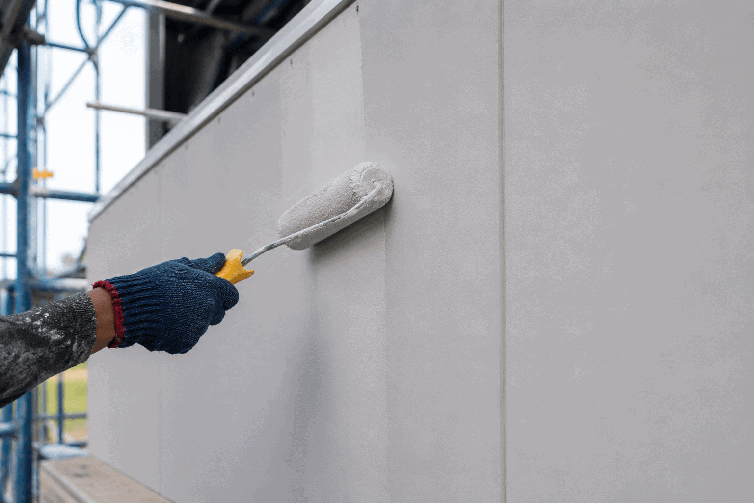Worker applying light gray paint with a roller on fiber cement boards to achieve a smooth premium painted finish