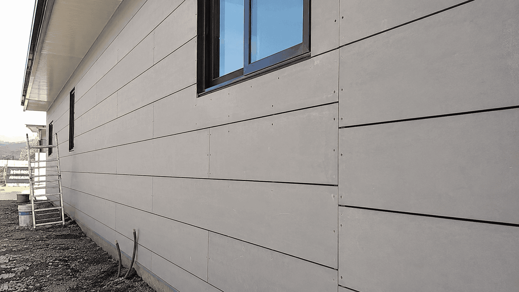 Fiber cement board wall with horizontal board layout, visible screw fixing, consistent joint gaps, and window openings during façade installation.